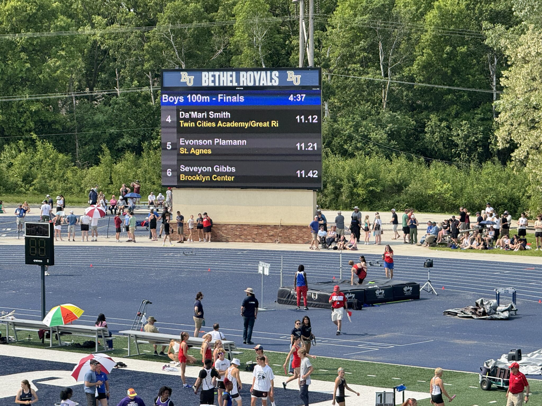 Track meet scoreboard with runners and spectators.